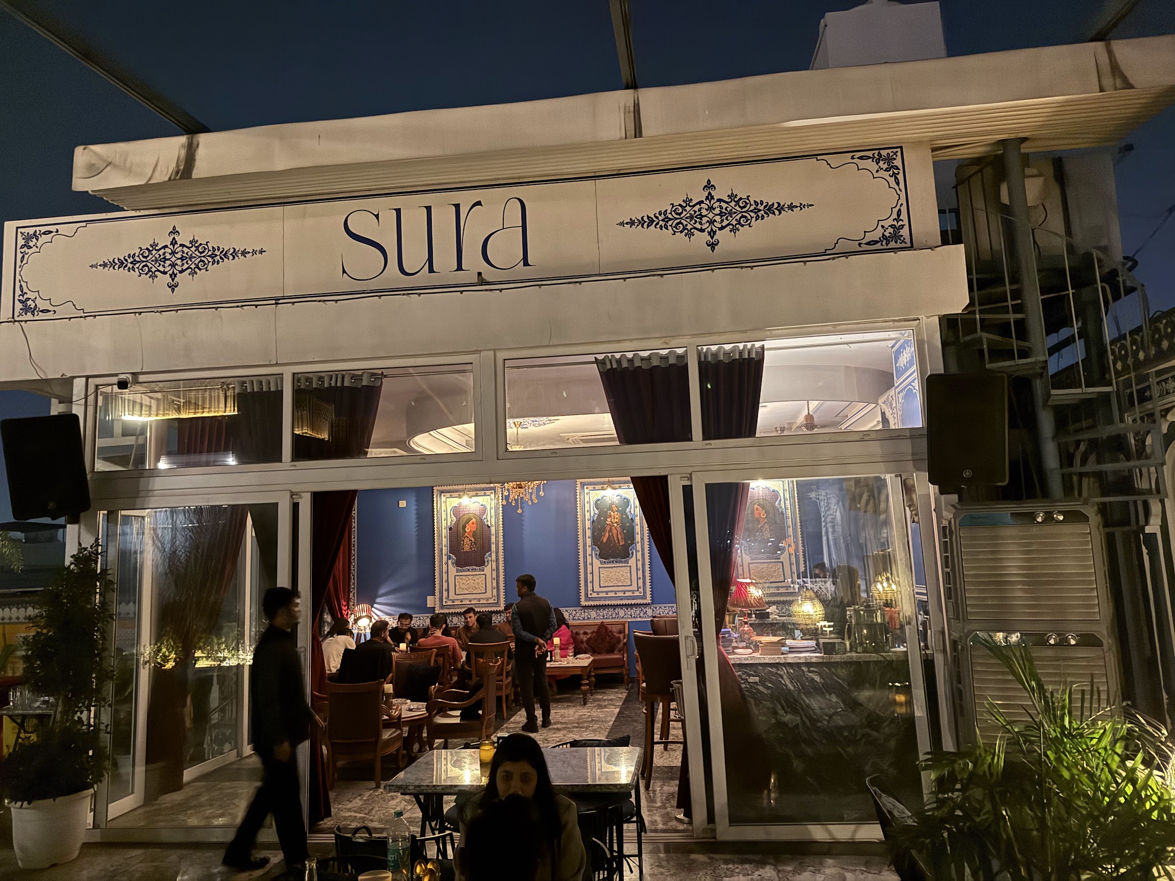 Guests on the Sura terrace at dusk, strung with warm lights